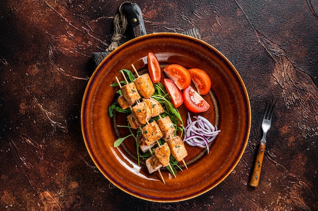 Brochetas de kebab de salmón a la barbacoa en plato rústico con verduras. Fondo oscuro. Vista superior.