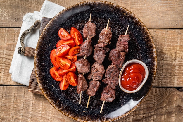 Brochetas de kebab de ternera a la parrilla o shashlik en un plato con tomate Fondo de madera Vista superior