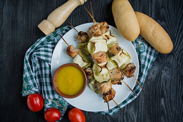 Brochetas en un pincho con calabacín con salsa, verduras y hierbas en un plato blanco.