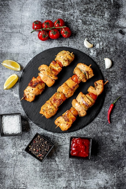 Brochetas de pollo en un plato negro con especias y limones