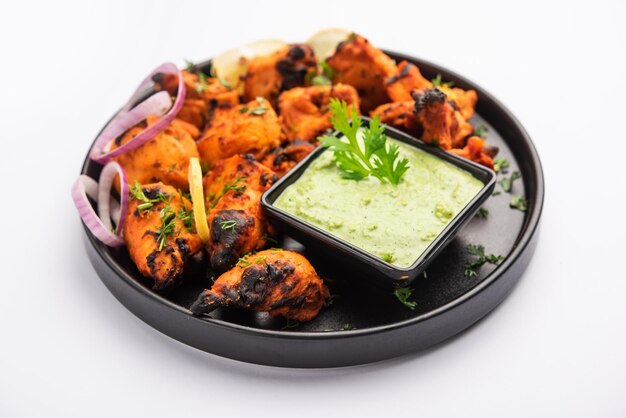 Brochetas de pollo tikka de la India, marinadas en especias y yogur y asadas en tandoor. servido con chutney verde y cebolla. enfoque selectivo