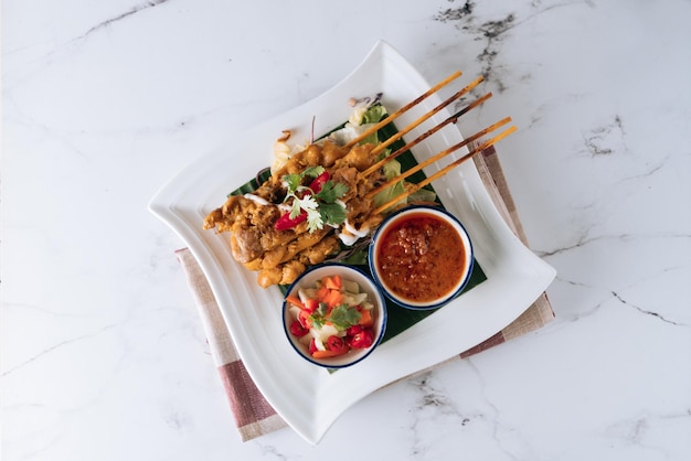 Brochetas satay de pollo de comida malaya tradicional con salsa de chile y ensalada en un plato aislado en la estera