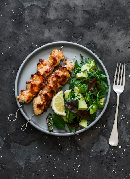 Brochetas de tocino de pollo y ensalada de acelgas, espinacas y rúcula de aguacate en una vista superior de fondo oscuro