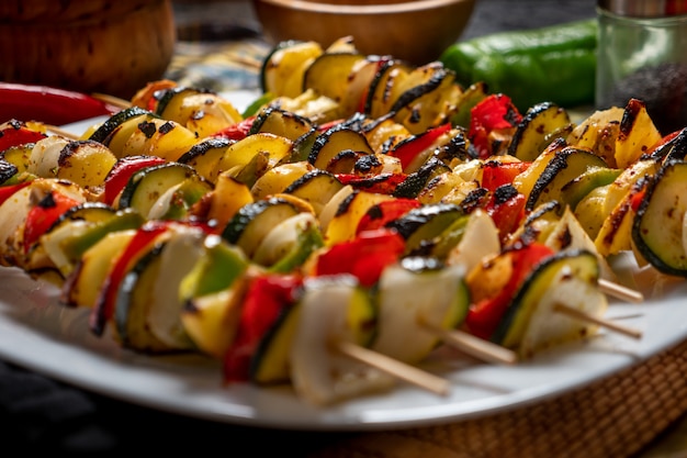 Brochetas de verduras en un plato blanco con algunos ingredientes crudos alrededor