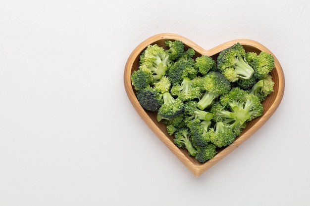 Brócoli fresco en un recipiente en forma de corazón sobre un fondo de madera | Foto Premium