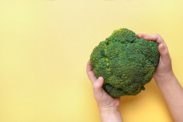 Brócoli en manos de los niños sobre un fondo amarillo