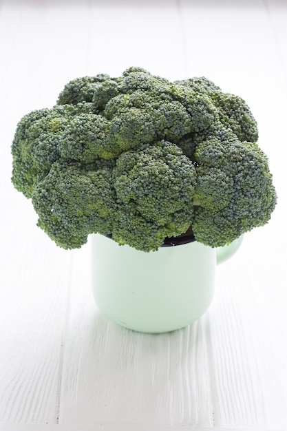 Brócoli verde en taza de té en una mesa de madera blanca