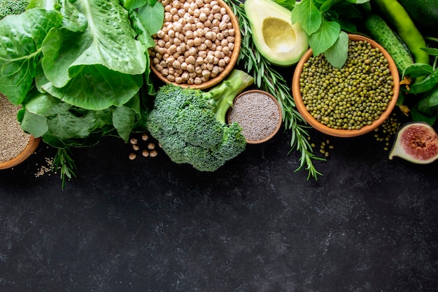 Brócolis, abacate, feijão mung, grão de bico, verduras em um fundo preto, vista superior. Conjunto de comida vegana.