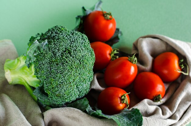 Brócolis e tomate crus frescos sobre fundo verde e tecido de linho. Comida orgânica.