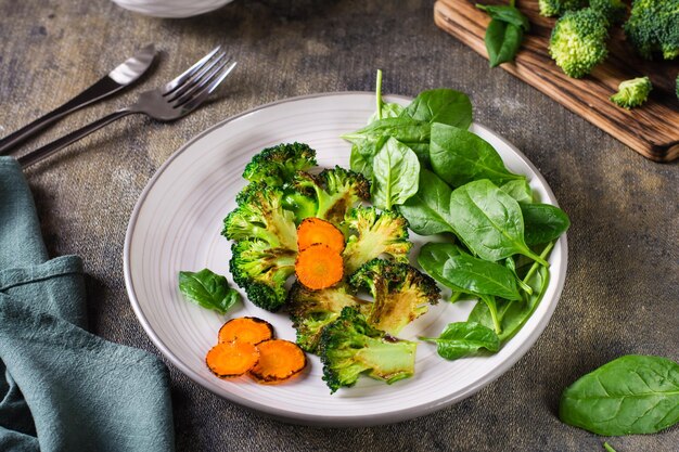 Brócolis grelhado e cenouras e folhas de espinafre frescas em um prato de dieta vegetal
