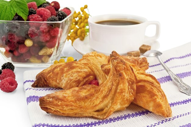 Brötchen in der gestreiften Serviette, Himbeeren, Brombeeren, Erdbeeren in einer Glasschüssel, Kaffee in einer weißen Tasse, Löffel, Rainfarnblüten einzeln auf weißem Hintergrund