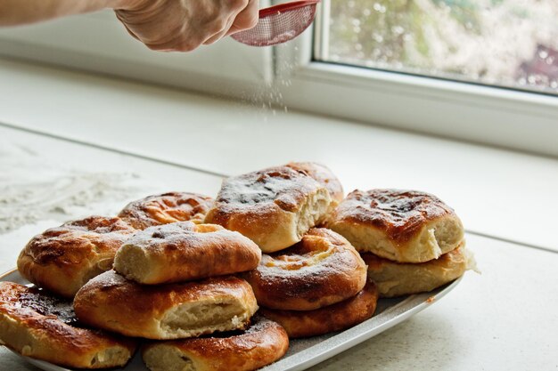 Foto brötchen in einem teller voller frisch gebackener käsekuchen eine weibliche hand, die mit zuckerpulver auf den küchentisch gestreut ist, kochen backen bühne der zubereitung von backrollen frühstück closeup kopierraum