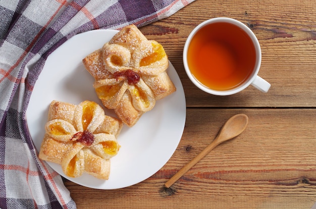 Brötchen mit Marmelade und Tasse Tee auf einem Holztisch