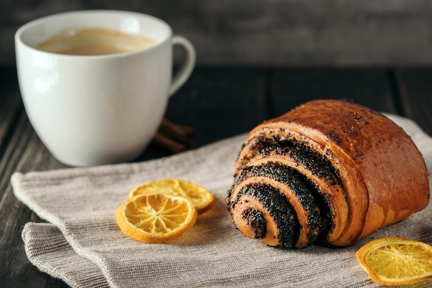 Brötchen mit Mohn und eine Tasse Kaffee auf dunklem Holzhintergrund mit Serviette