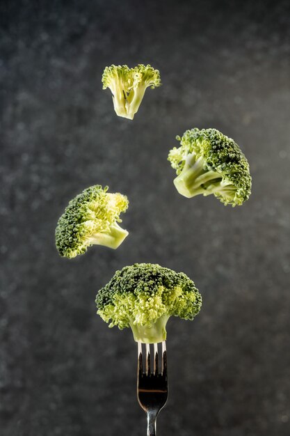 Foto brokkoli auf einer gabel und levitation gemüse auf einem dunklen hintergrund gesundes lebensmittelkonzept