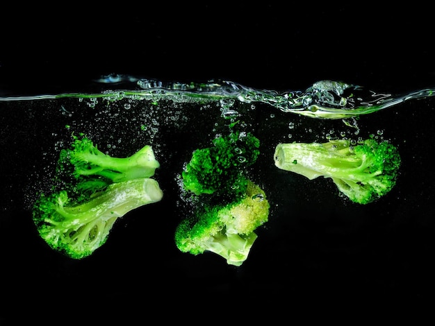 Brokkoli fällt in das kochende Wasser auf dunklem Hintergrund Unterwasseransicht Kochen vegetarischer Koch