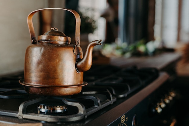 Bronzekessel in der modernen Küche. Alte Vintage Teekanne auf Gasherd. Tee zubereiten. Wasserkocher aus Aluminium. Sonniges Tageslicht vom Fenster.