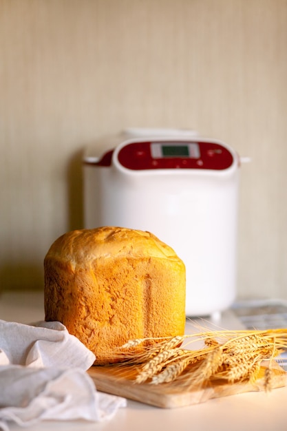 Brot aus einer Brotbackmaschine mit Weizenährchen auf einem Brett mit einer Küchenserviette