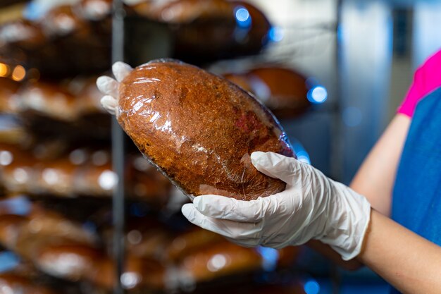 Brot in den Händen eines Bäckers auf dem Hintergrund eines Industrieofens und Regale mit Brot. Industrielle Brotproduktion.