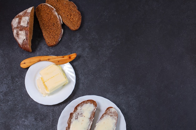 Brot mit Butter mit einem hölzernen Buttermesser auf schwarzem Hintergrund