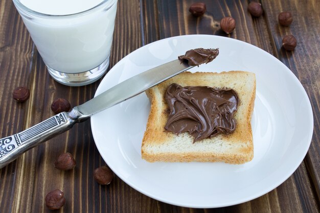 Brot mit Schokoladencreme und Milch auf dem Holzhintergrund