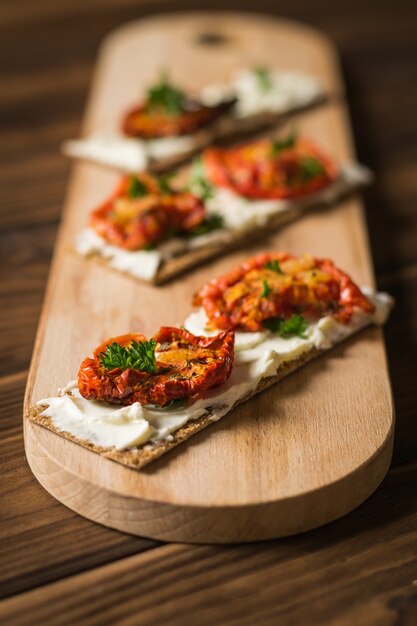 Brot Toast mit Frischkäse und sonnengetrockneten Tomaten auf einem Schneidebrett.