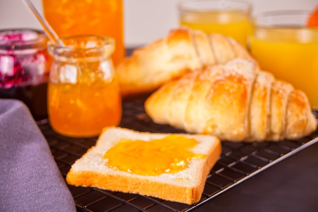 Brot Toast mit Orangenmarmelade, frischen Croissants Brötchen, Gläser Orangensaft. Frühstückskonzept.