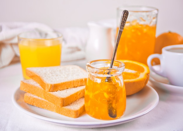 Brot Toast mit Orangenmarmelade, Gläser Orangensaft auf dem weißen Tisch Frühstückskonzept.