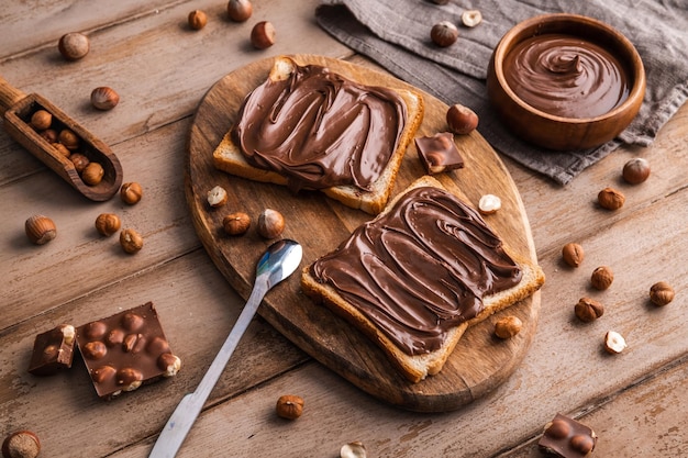 Brotbrett mit Schokoladenpaste und Haselnüssen auf Holzhintergrund