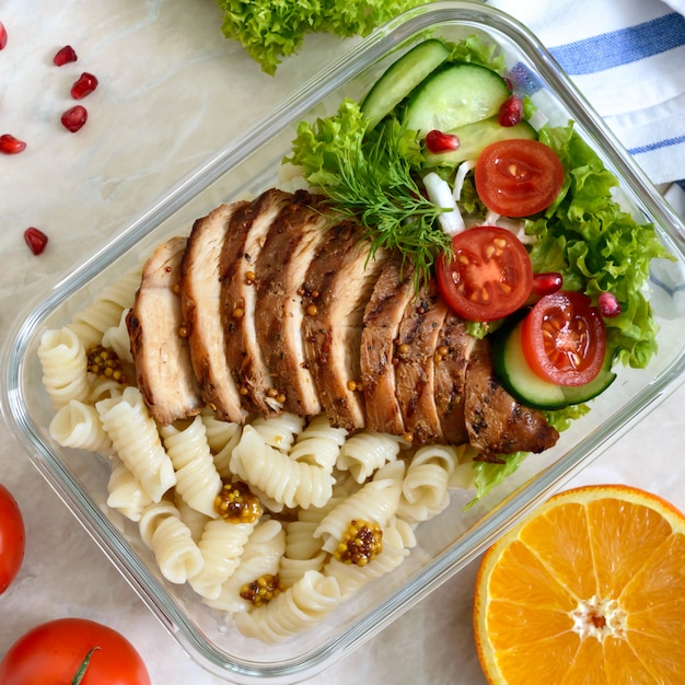 Brotdose: Rotini mit gebackener Hähnchenbrust und Salat. Draufsicht, flach liegen. Leckeres gesundes Mittagessen.
