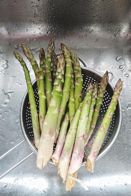 Brote de espárragos verdes frescos lavados en colador de acero en el fregadero de la cocina vista anterior