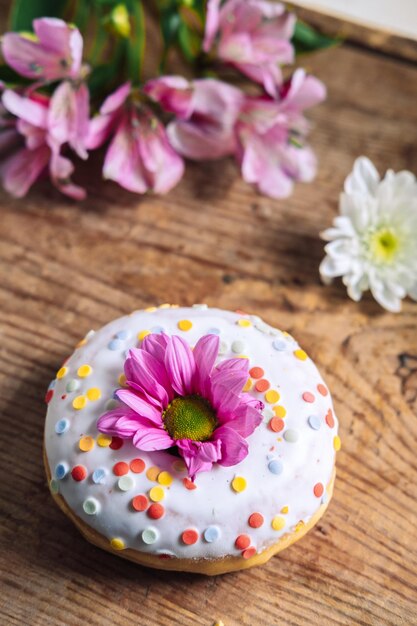 Foto brote de manzanilla en la parte superior de una rosquilla en un fondo de madera con un ramo de alstroemerias marco delicado con flor rosa.