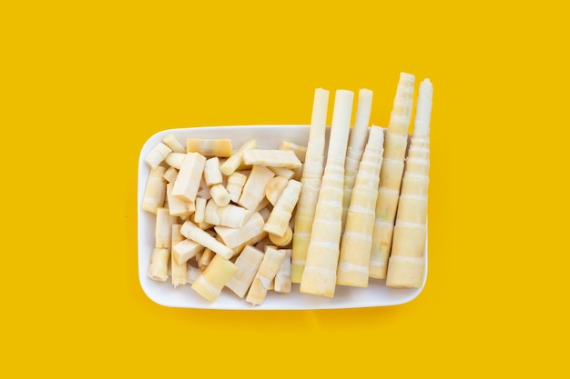Brotes de bambú en plato blanco sobre fondo amarillo.