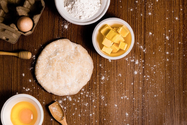 Brotkonzept ein Brötchenteig, ein kleiner Holzspatel, eine Schüssel Mehl und eine Schüssel mit einem rohen Ei