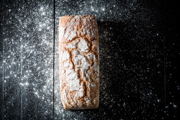 Brotlaib auf schwarzem Tisch mit Mehl