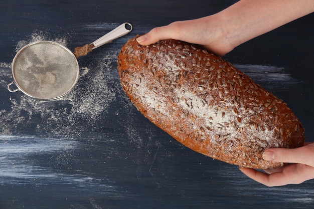 Brotlaib frisch in weiblichen Händen auf farbigem Holztischhintergrund