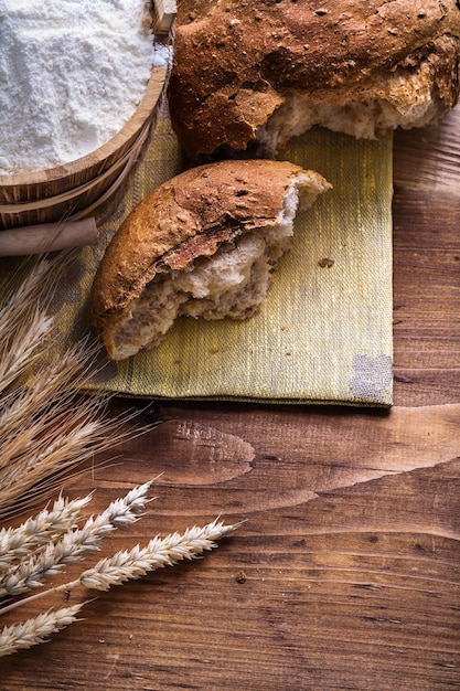 Brotscheibe mit Ähren und Mehl im Eimer auf altem Holzbrett