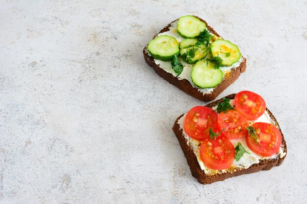 Brotscheiben mit Gurken und Tomaten auf konkretem Hintergrund