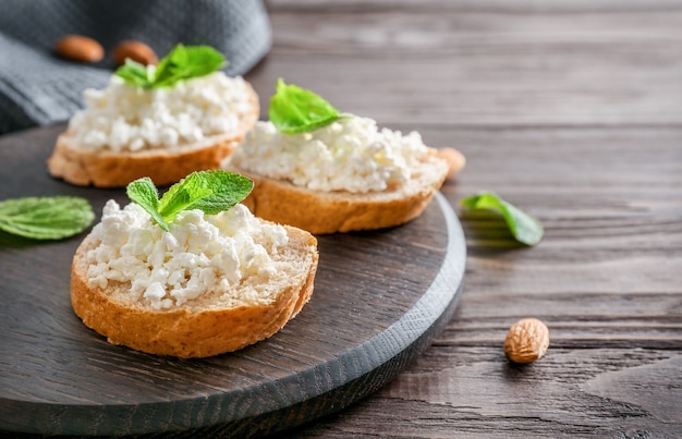 Brotscheiben mit Hüttenkäse und Minzblättern auf Holzbrett auf Holzhintergrund.