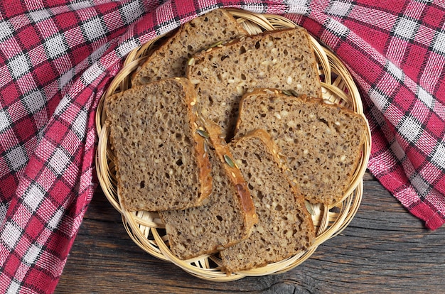 Brotscheiben mit verschiedenen Samen in Weidenteller auf Holztisch und roter Tischdecke, Ansicht von oben