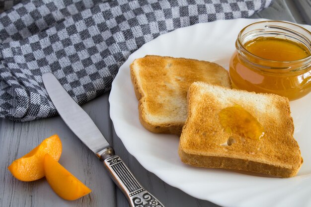 Brottoast mit Aprikosenmarmelade in der weißen Platte auf dem grauen Holzhintergrund