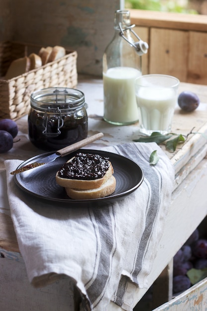 Brottoast mit Pflaumenmarmelade, serviert mit Milch und Pflaumen. Rustikaler Stil.