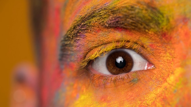 Brown-Auge des jungen Mannes mit hellem Holi künstlerischem Make-up