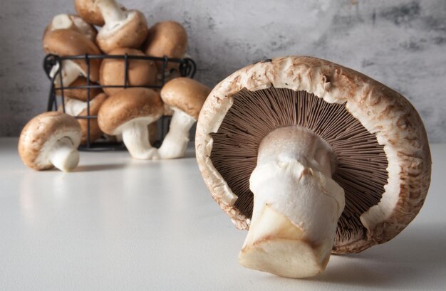 Brown Cap Champignon auf dem Tisch vor dem Hintergrund eines Korbes mit Pilzen aus nächster Nähe