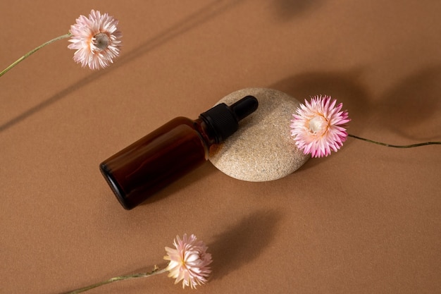 Brown Glasflaschentropfer mit kosmetischem Öl mit rosa trockenen Blumen auf Terrakotta-Hintergrund Vorderansicht, Nahaufnahme