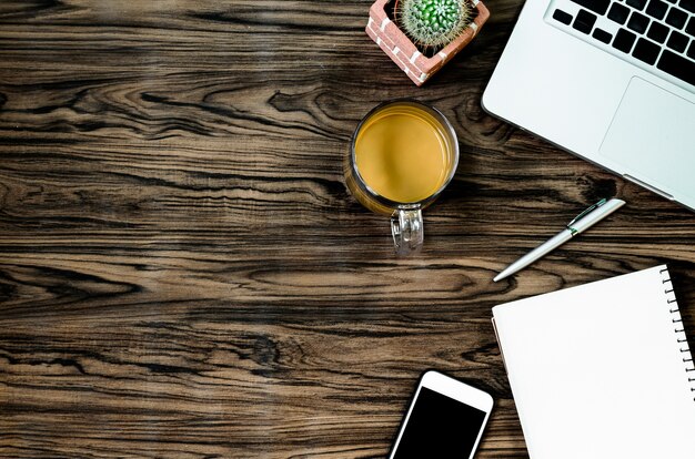 Brown-hölzerne Büroschreibtischtabelle mit einem Buch, einem Stift, einem Kaktus und einem Telefon für das Arbeiten in der Draufsicht.