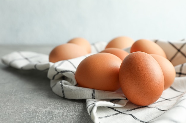 Brown huevos de gallina en una toalla de cocina en la mesa gris contra la luz