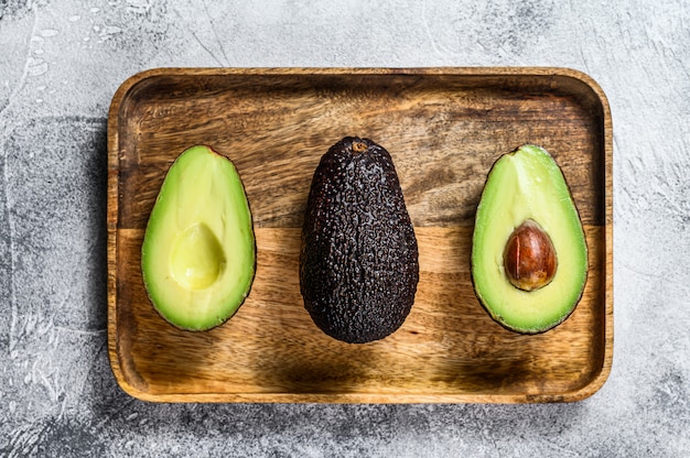 Brown-reife Avocadohälften auf einem hölzernen hackenden Brett. Grauer Hintergrund. Ansicht von oben