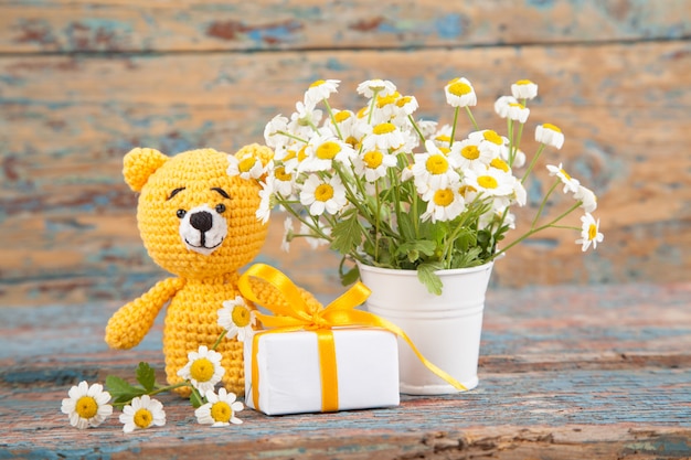 Brown strickte kleinen Bären mit Kamille auf einem alten hölzernen Hintergrund. Handgemachtes, gestricktes Spielzeug. Amigurumi