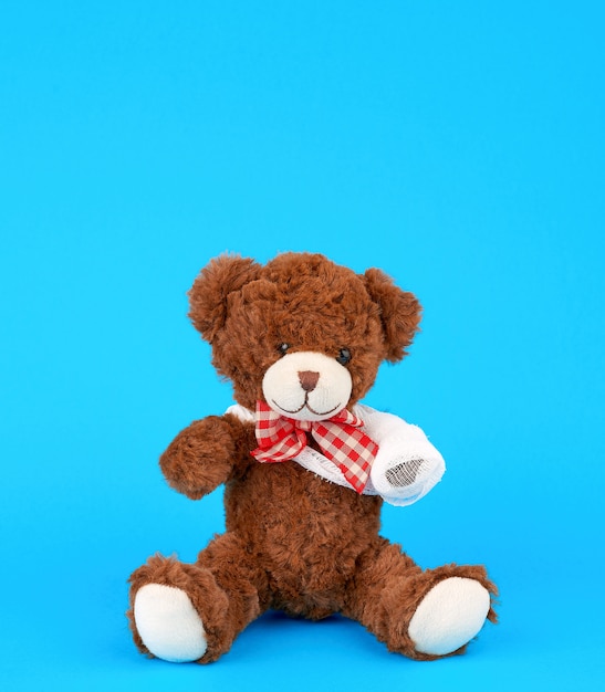 Brown-Teddybär mit der zurückgewickelten weißen Verbandpfote auf einem blauen Hintergrund